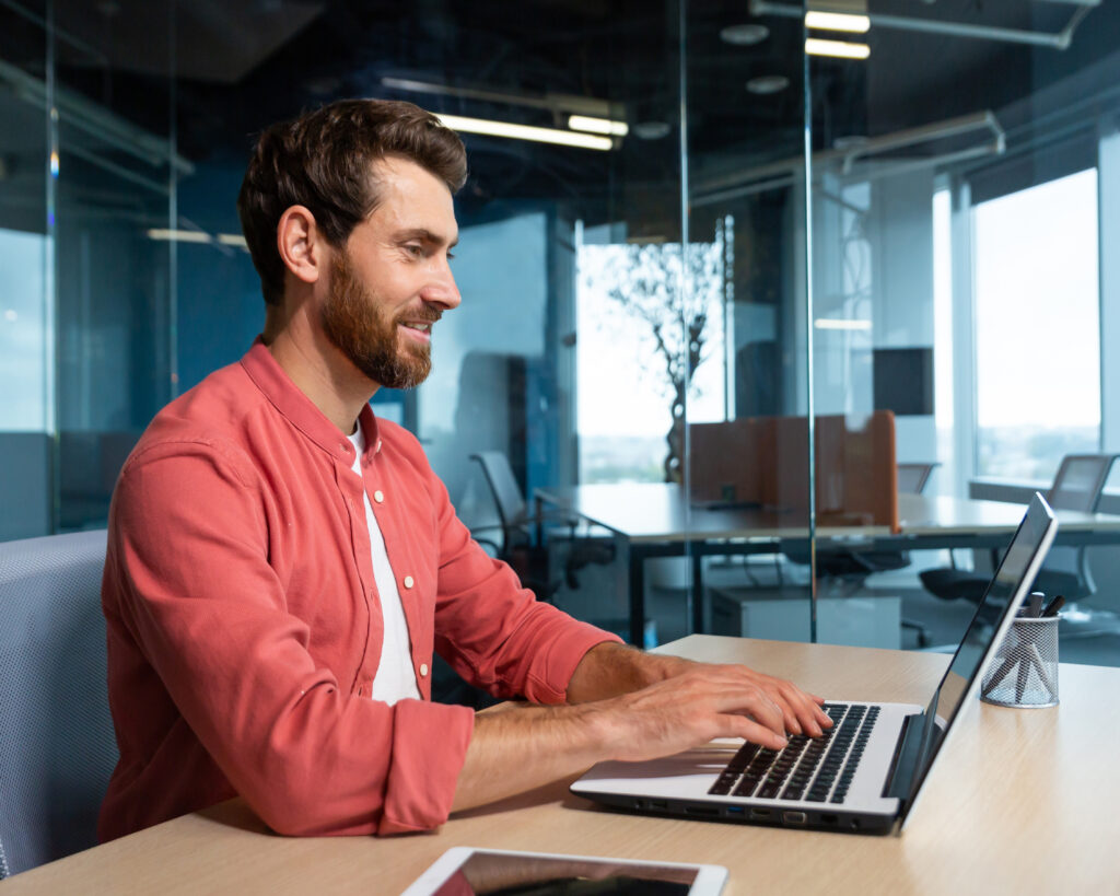 Smiling man using computer laptop in office setting