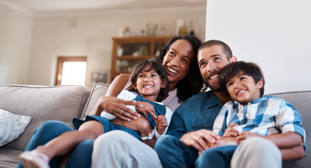 Image of happy family with young daughter and son, mother and father sitting on sofa and watching CDE lightband digital services