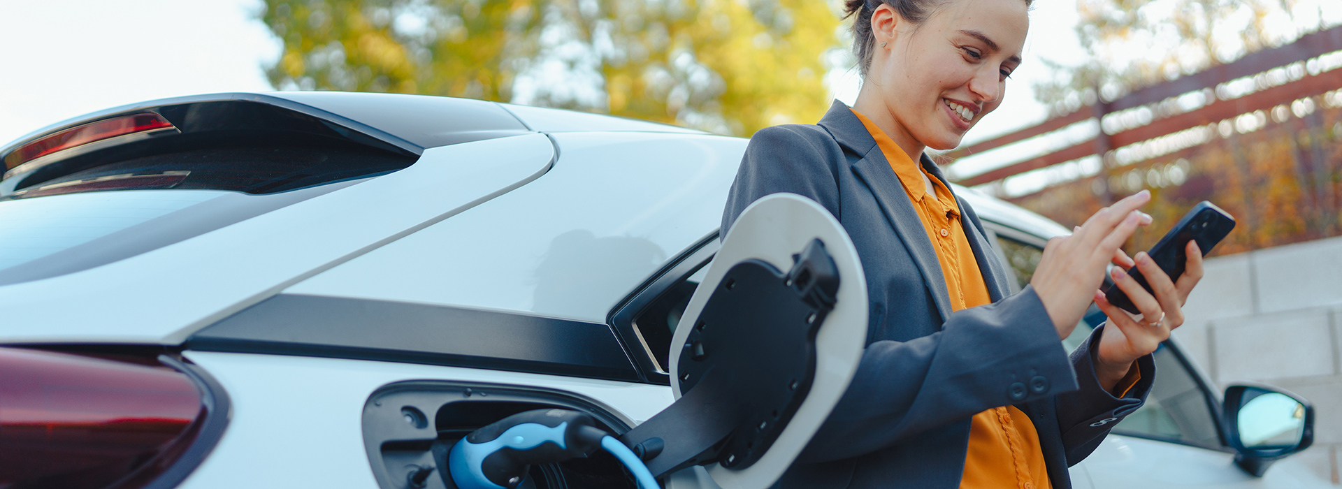 Image of women, smiling, and passing some time using a mobile device while charging her electric vehicle