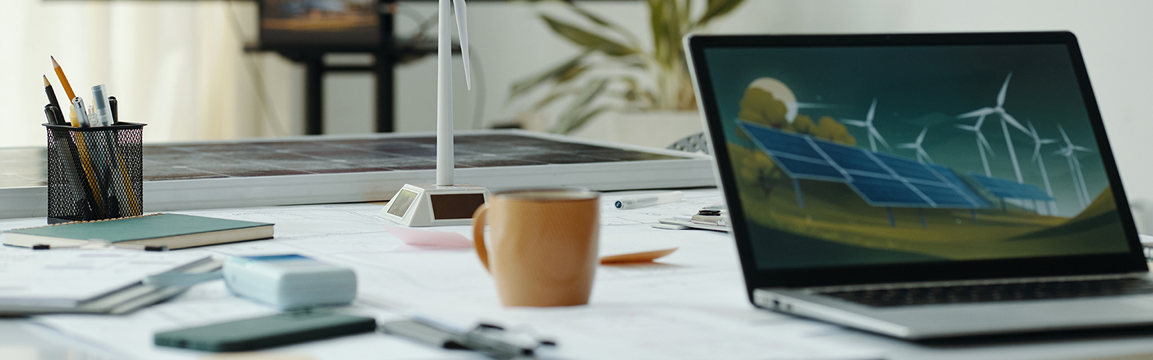 An image of a desk with a laptop, computer, coffee, cup, and model of wind turbine for wind energy