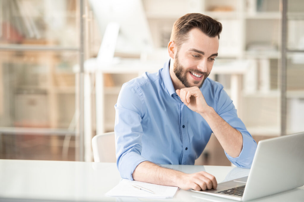 Image of man at corporate office, smiling while using laptop computer on high speed business Internet
