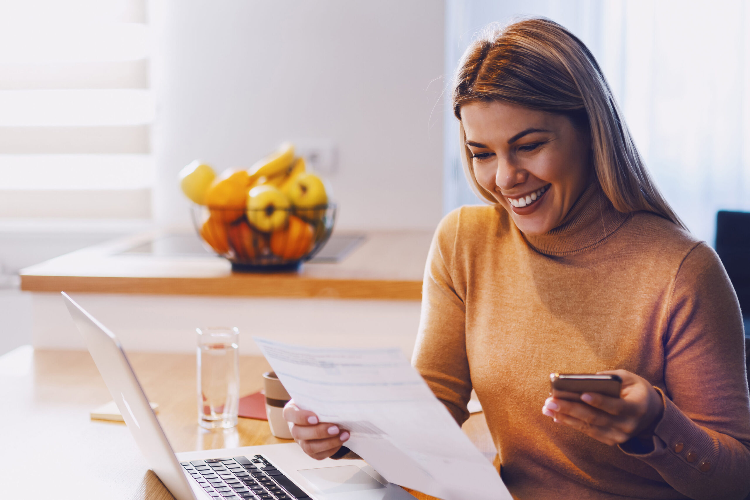 Woman, smiling reviewing her bill online from mobile phone and laptop