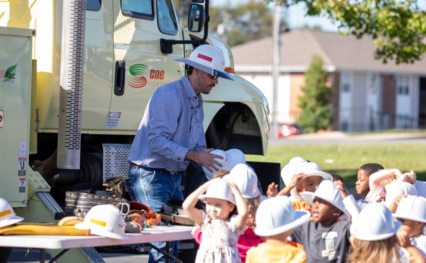 Electric lineman hands out hats to young children.